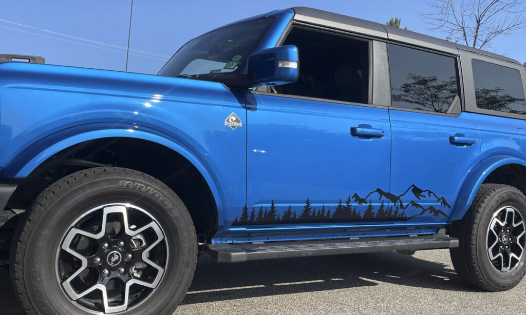 Blue Jeep Wrangler with black custom mountain decal, highlighting premium vinyl wraps and custom car graphics installation for Jeep dealerships.